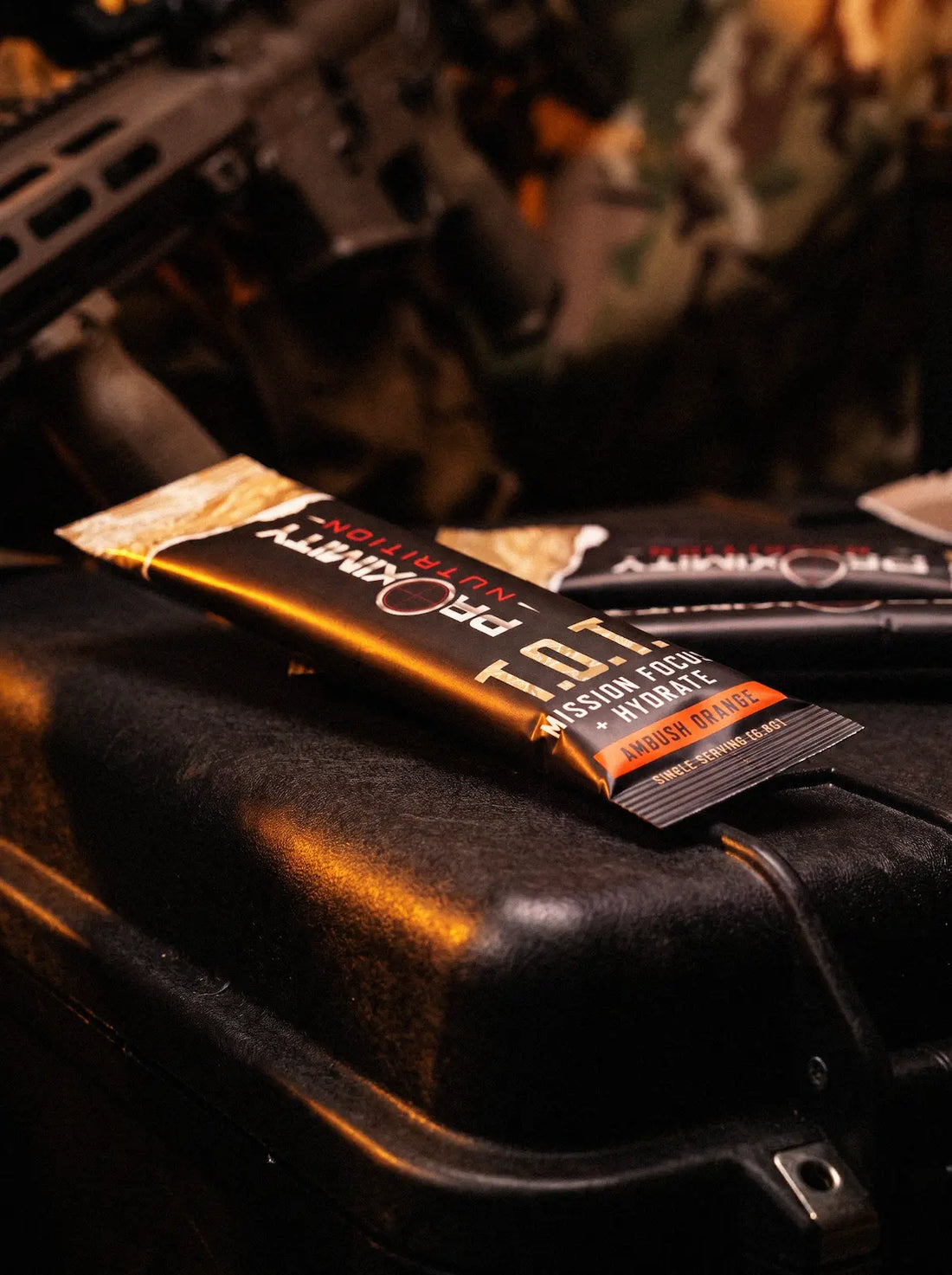 T.O.T. Ambush Orange stick packs on a black equipment case with camouflage gear behind them.