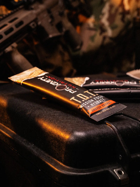 T.O.T. Ambush Orange stick packs on a black equipment case with camouflage gear behind them.