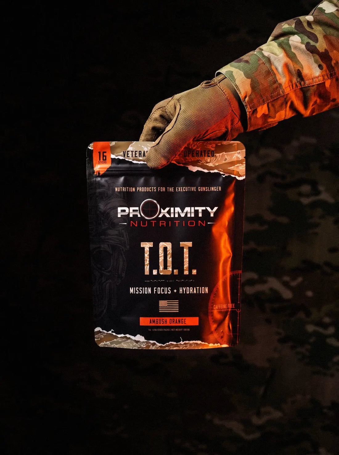Gloved hand holding a T.O.T. Ambush Orange pouch against a camouflage background.